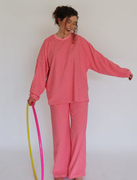 A woman modeling a pink striped lounge set, consisting of a long-sleeve top and matching pants, while holding a pink and yellow and pink hula hoop against a plain white background.