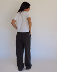 Person wearing dark gray pants with blue stripes and a white shirt against a plain background