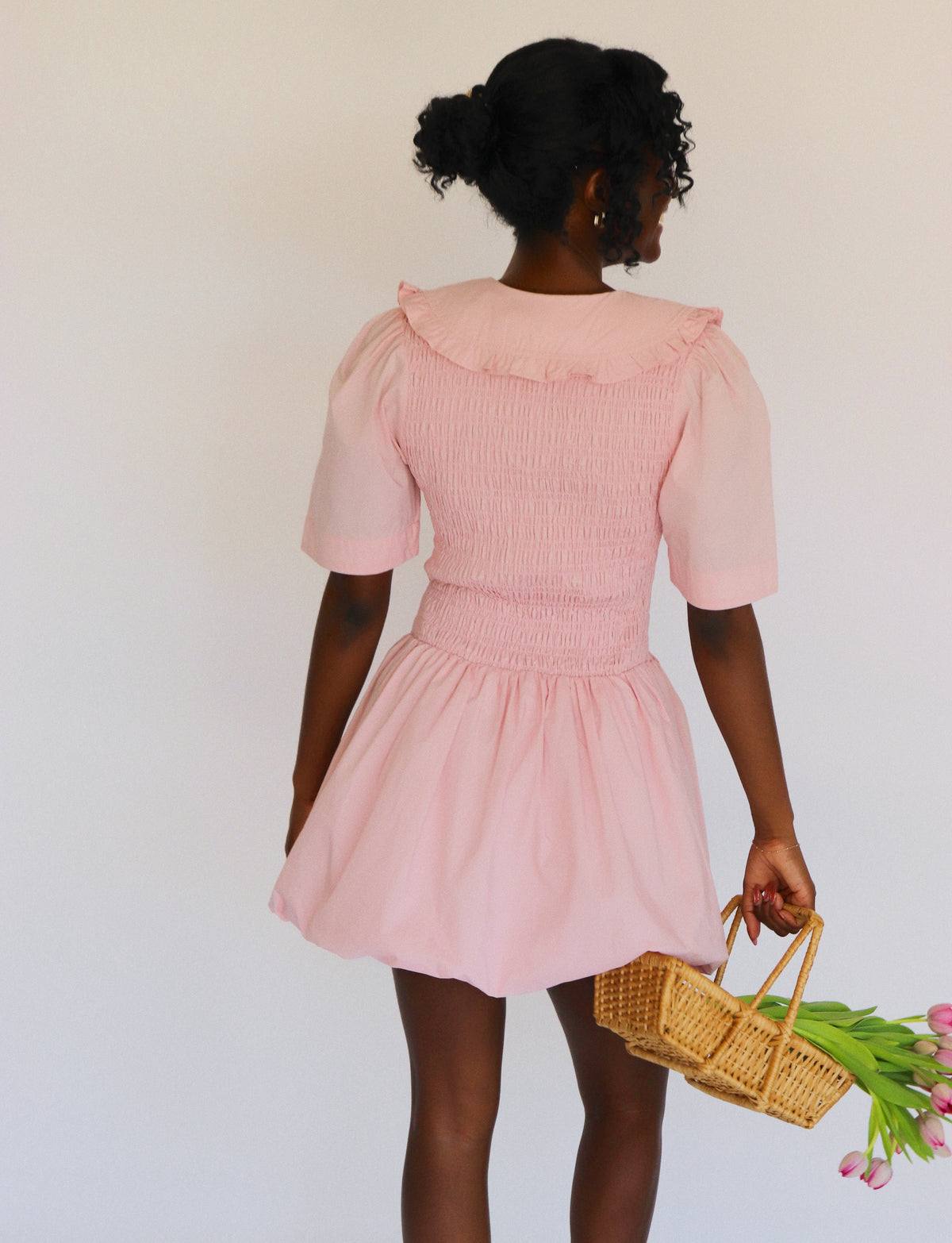 Woman wearing a pink dress holding a basket of flowers against a white background