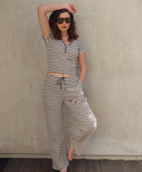 Woman wearing a dark gray and white striped outfit against a plain wall.