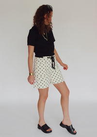 Woman wearing a black crop top and polka dot shorts against a plain background