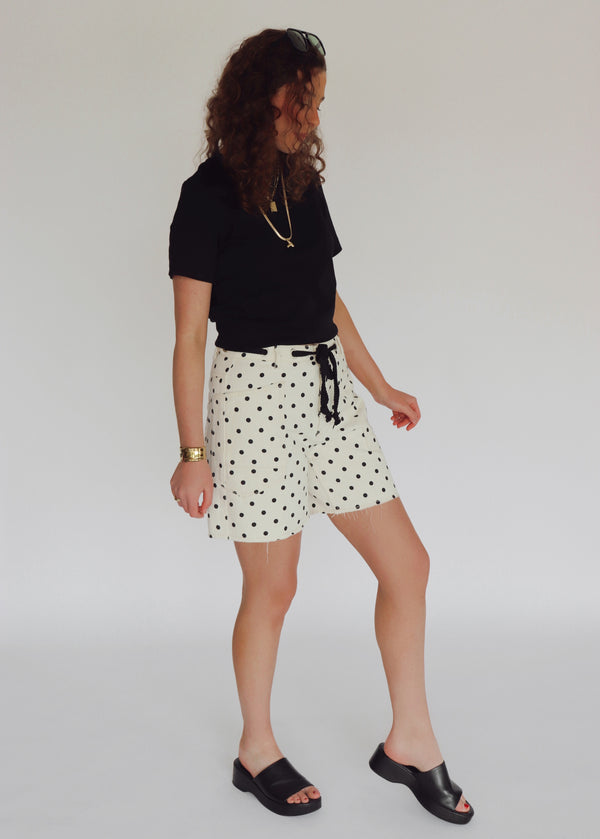Woman wearing a black crop top and polka dot shorts against a plain background