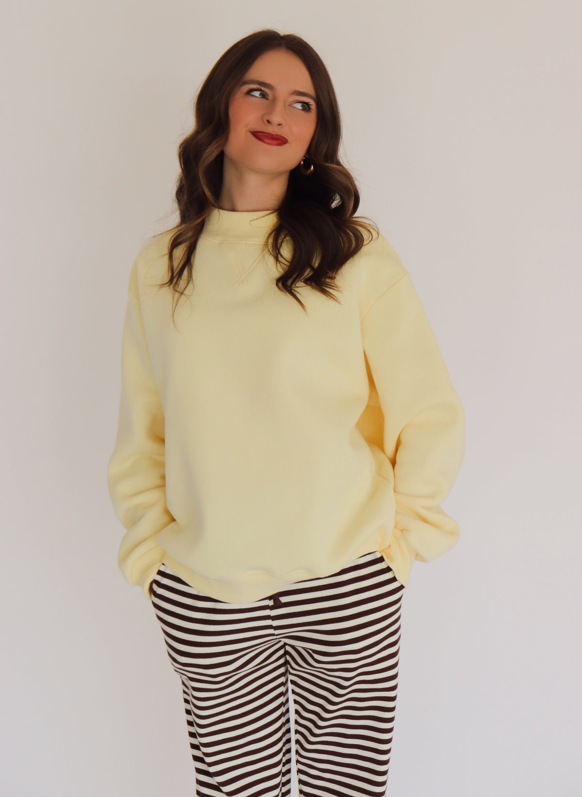 Woman wearing a light yellow pullover and striped pants against a plain background