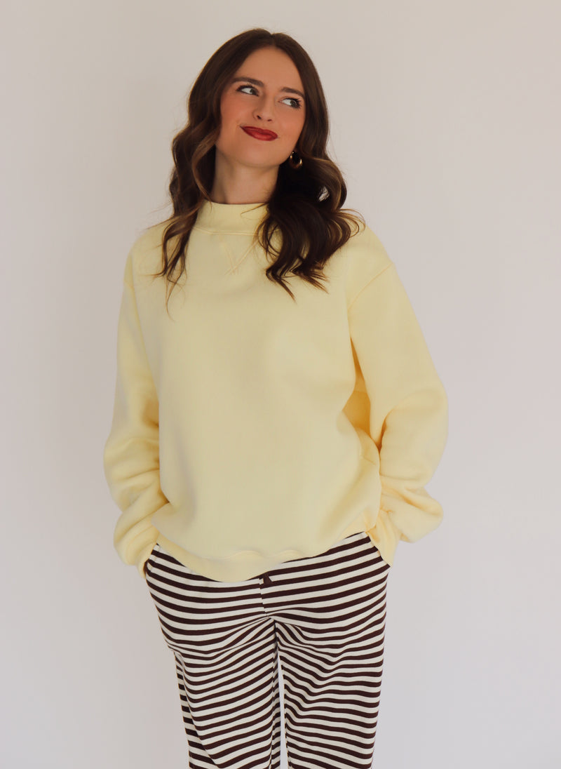 Woman wearing a light yellow pullover and striped pants against a plain background