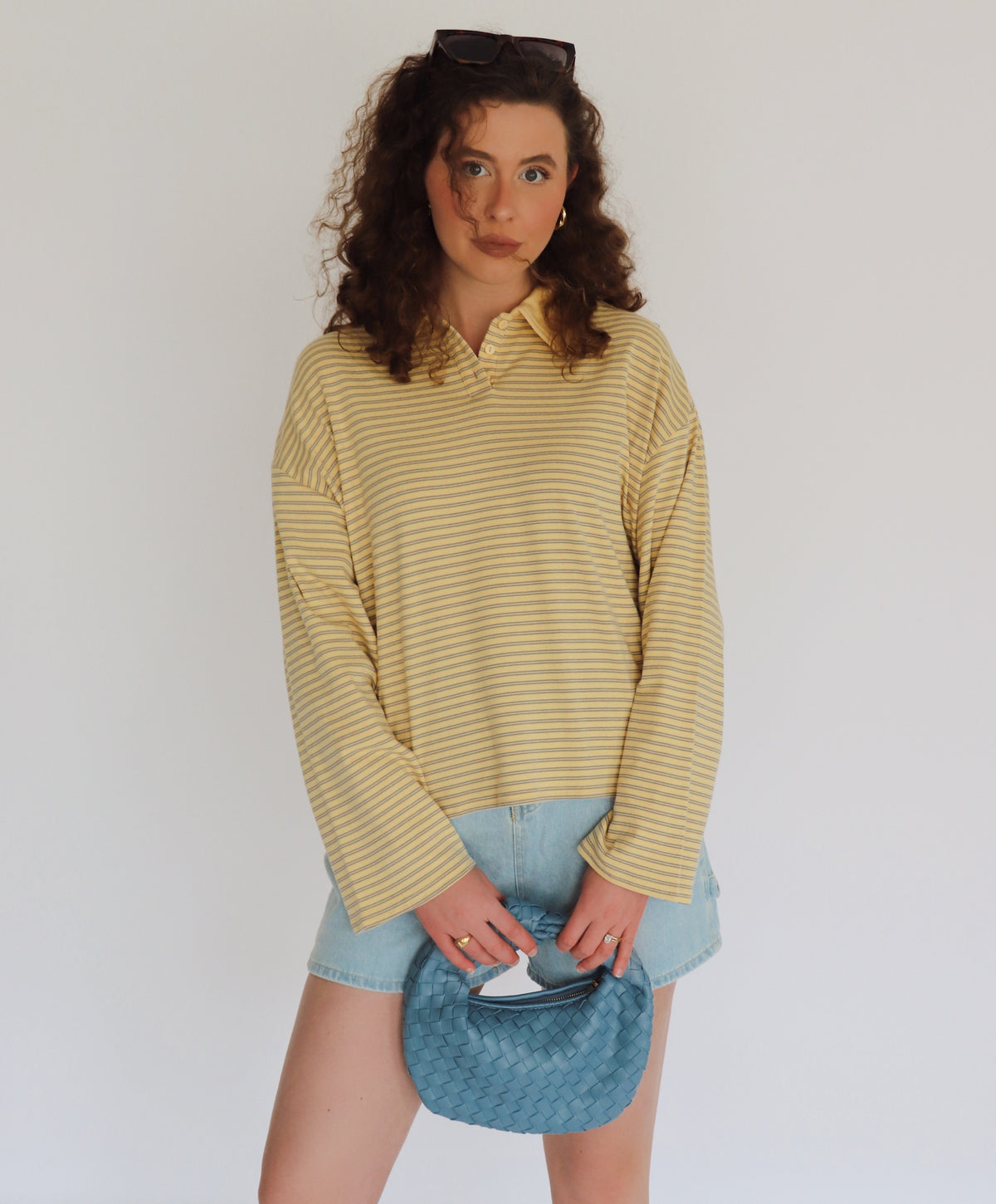 Woman wearing a yellow striped shirt and denim shorts holding a blue bag against a white background