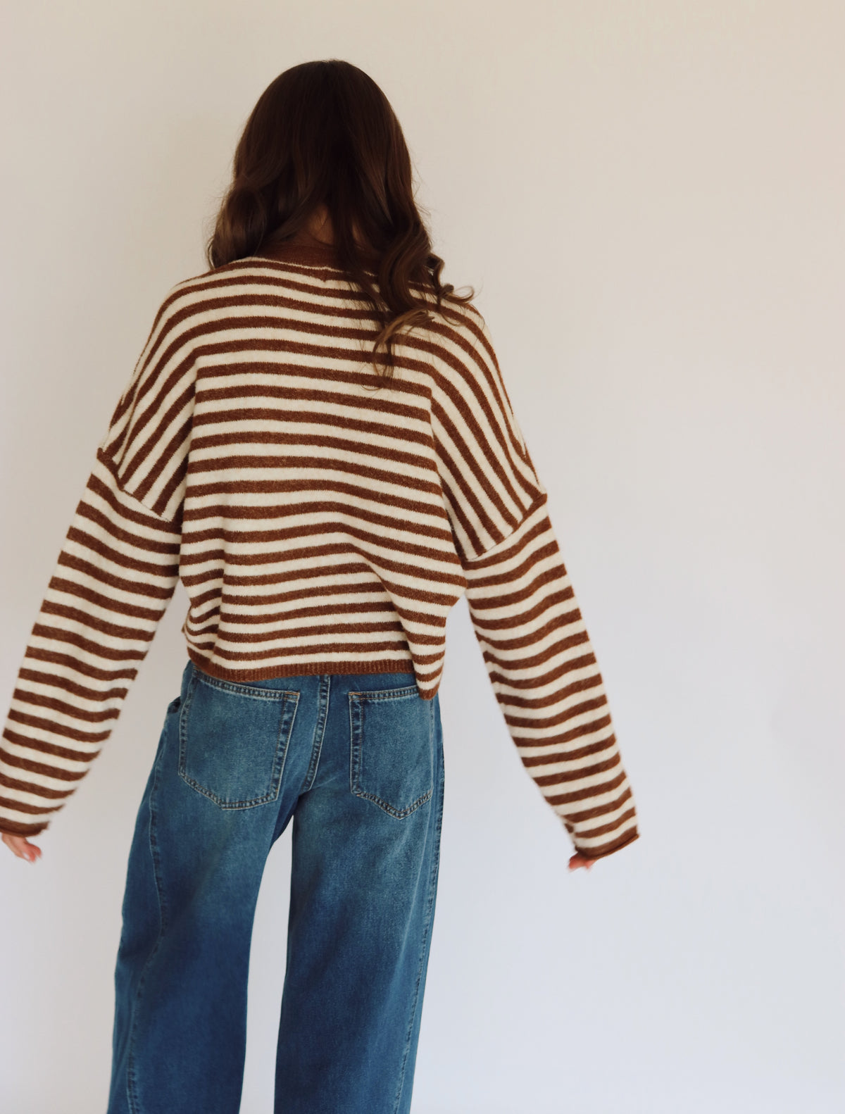 Woman wearing a brown and white striped sweater cardigan and blue jeans in front of  a white background