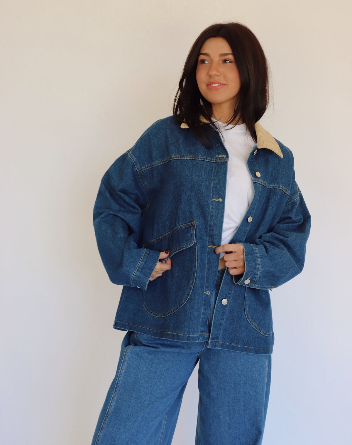 Person wearing a blue denim jacket and denim pants against a white background