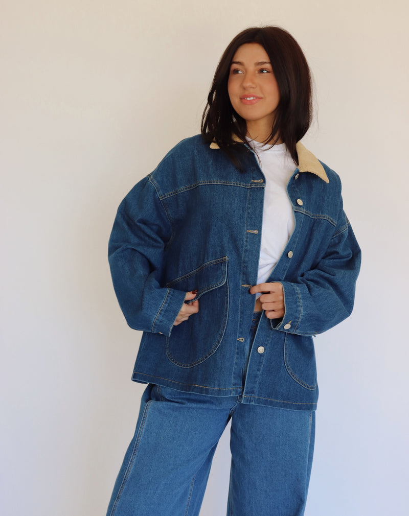Person wearing a blue denim jacket and denim pants against a white background