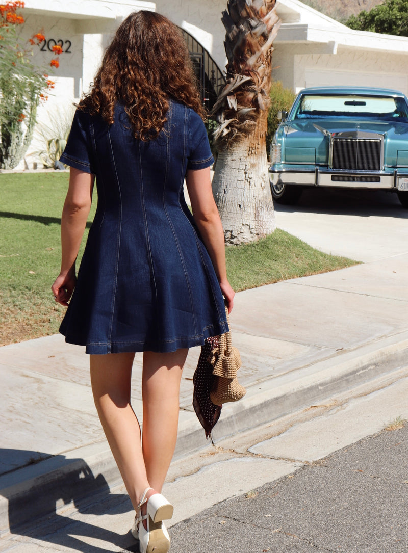 Woman in a blue dress walking near  a sidewalk with a vintage car in the background.