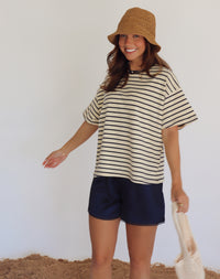 Woman wearing a striped shirt and shorts with a straw hat against a white background
