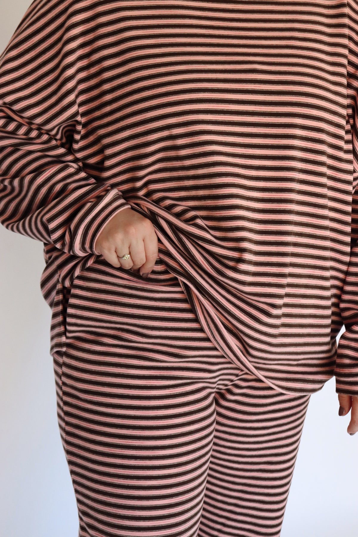 Woman wearing a brown and pink striped loungewear set in front of an off white wall.