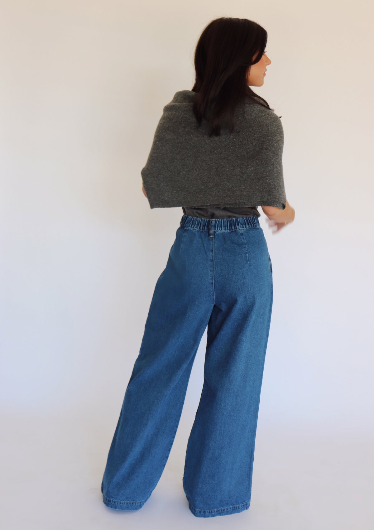 Woman wearing a dark gray turtleneck, a cardigan and blue jeans against a white background