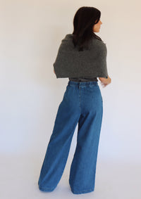 Woman wearing a dark gray turtleneck, a cardigan and blue jeans against a white background