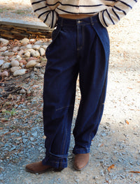 A person wearing dark blue high-waisted wide-leg denim jeans with rolled cuffs, paired with a cream and navy striped long-sleeve top and brown boots, standing outdoors on a gravel path.
