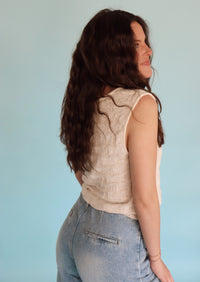 Woman wearing a vest and jeans against a plain background