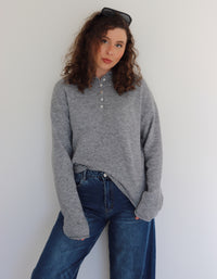 Woman wearing a gray top  and blue jeans against a white wall