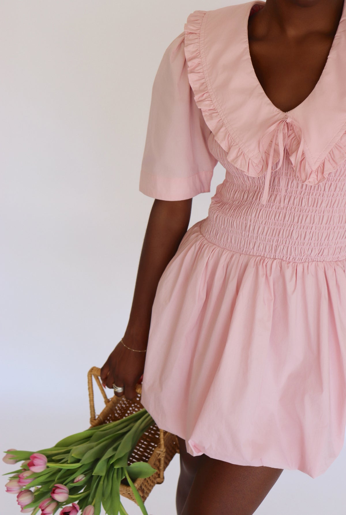 Woman wearing a pink dress holding a basket of flowers against a white background