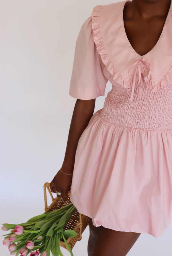 Woman wearing a pink dress holding a basket of flowers against a white background