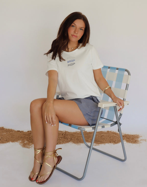 Woman sitting on a striped chair wearing a white t-shirt and shorts.