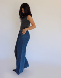 Woman wearing a dark gray turtleneck and blue jeans against a white background
