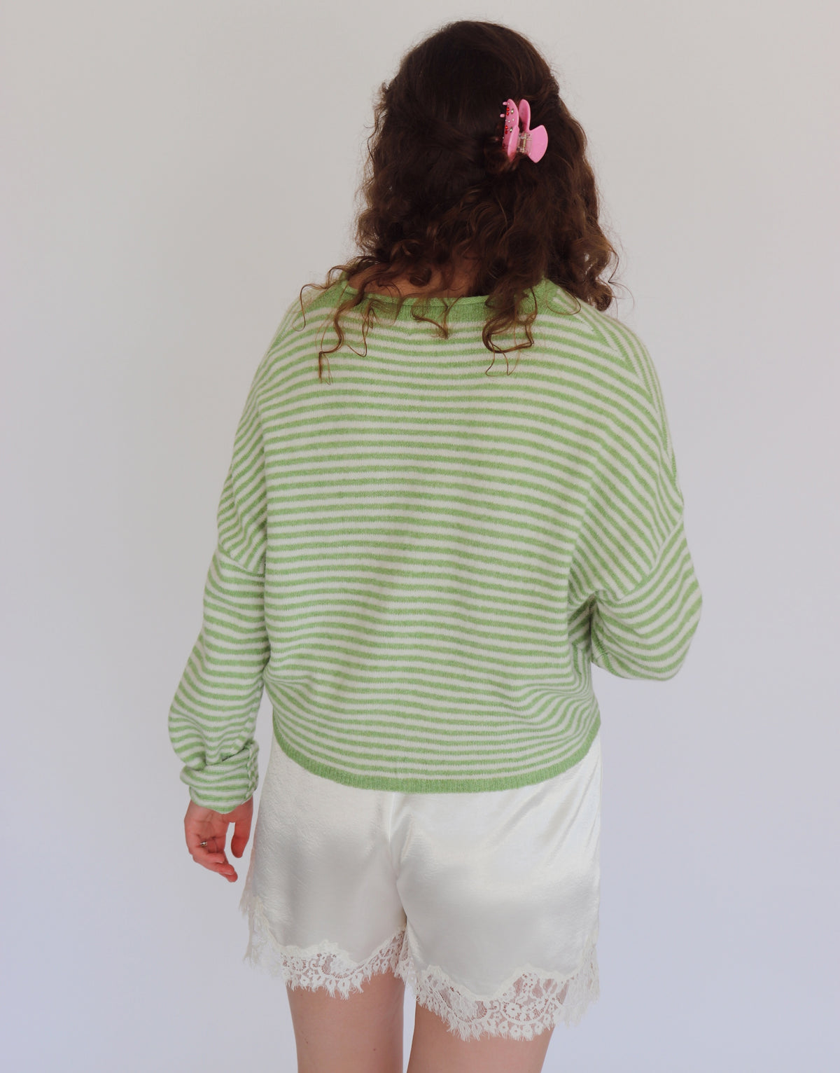 A person shown from the back wearing a light green and white striped long-sleeve top and white satin shorts with lace trim, against a plain light gray background.