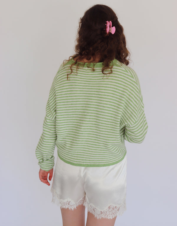 A person shown from the back wearing a light green and white striped long-sleeve top and white satin shorts with lace trim, against a plain light gray background.