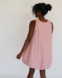 Woman wearing a pink dress with white polka dots on it against a white background