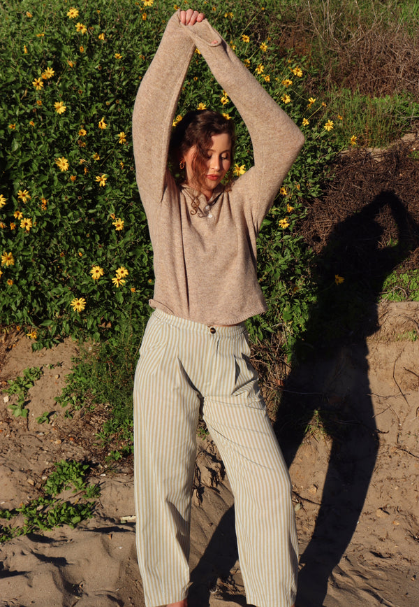 Person outdoors with greenery and flowers in the background wearing a brown top and striped pants.
