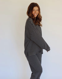 A woman modeling a matching two-piece loungewear set consisting of a long-sleeve top and wide-leg pants, both featuring a navy and white horizontal stripe pattern, set against a plain white studio background.