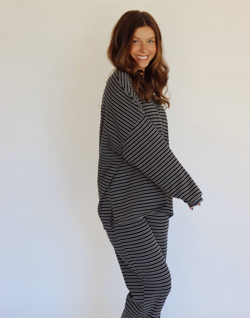 A woman modeling a matching two-piece loungewear set consisting of a long-sleeve top and wide-leg pants, both featuring a navy and white horizontal stripe pattern, set against a plain white studio background.