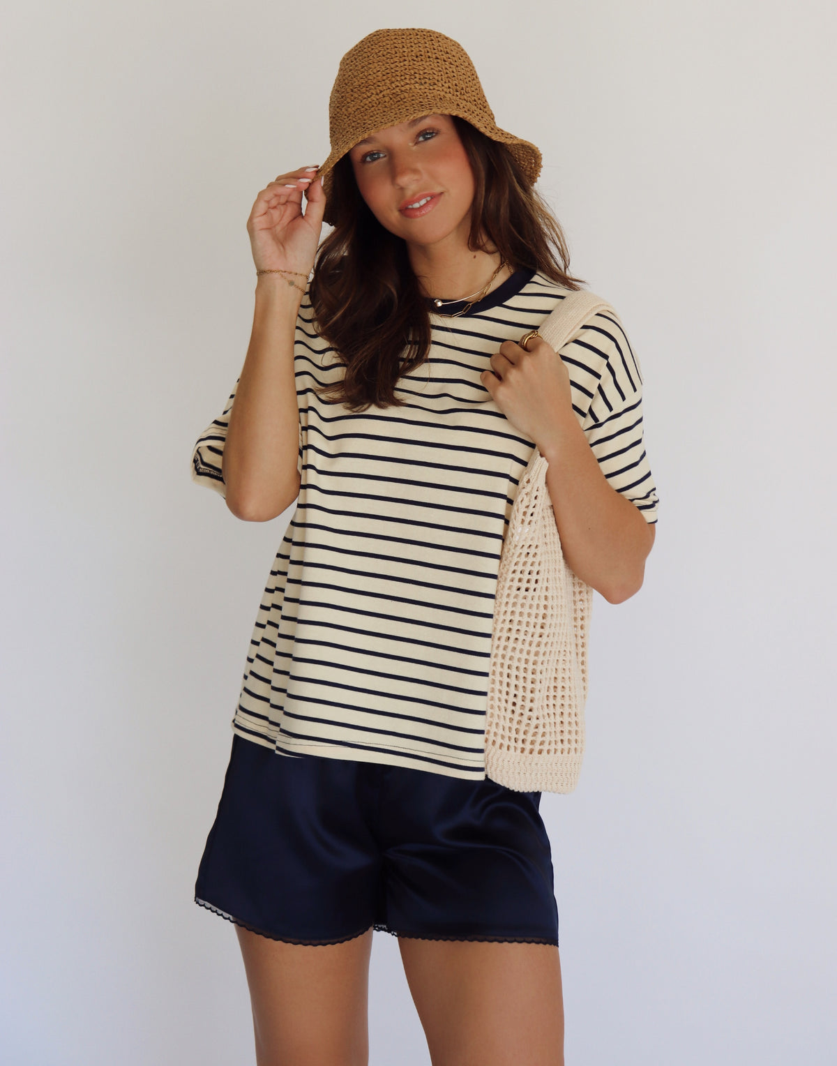 Woman wearing a striped shirt and shorts with a straw hat against a white background