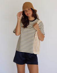 Woman wearing a striped shirt and shorts with a straw hat against a white background