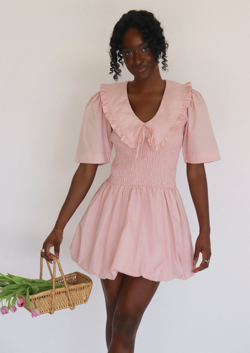 Woman wearing a pink dress holding a basket of flowers against a white background