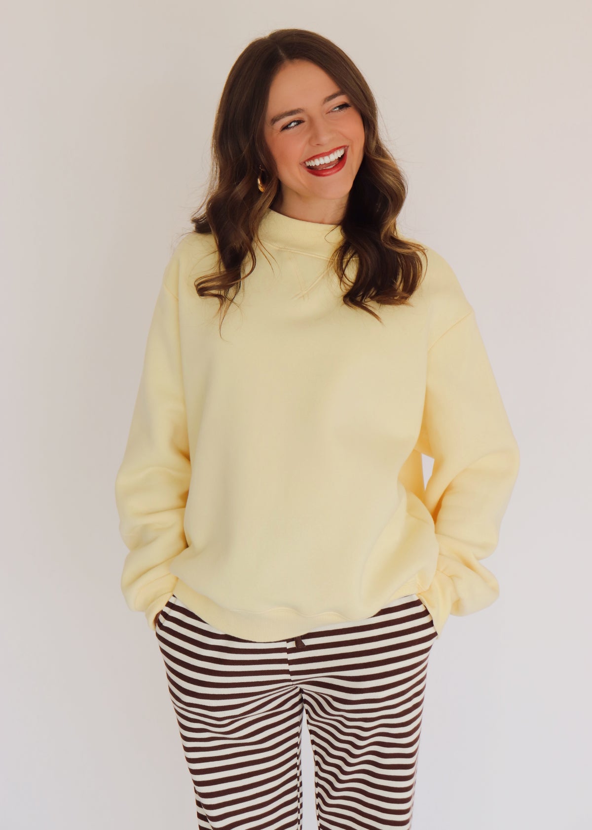 Woman wearing a light yellow pullover and striped pants against a plain background