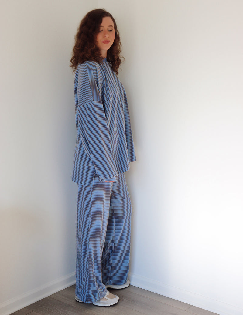 Person wearing a blue striped outfit standing against a white wall.