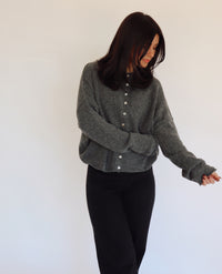Woman wearing a gray sweater cardigan with button details against a white background