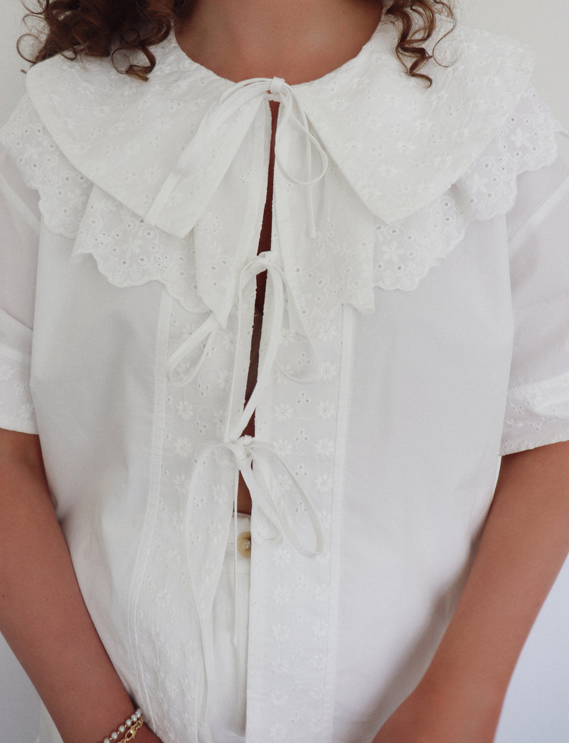 White blouse with eyelet details on a plain background