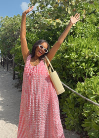 Woman in a pink dress with arms raised in front of green foliage
