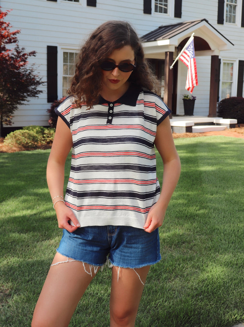Woman wearing a striped shirt and denim shorts standing in front of a house