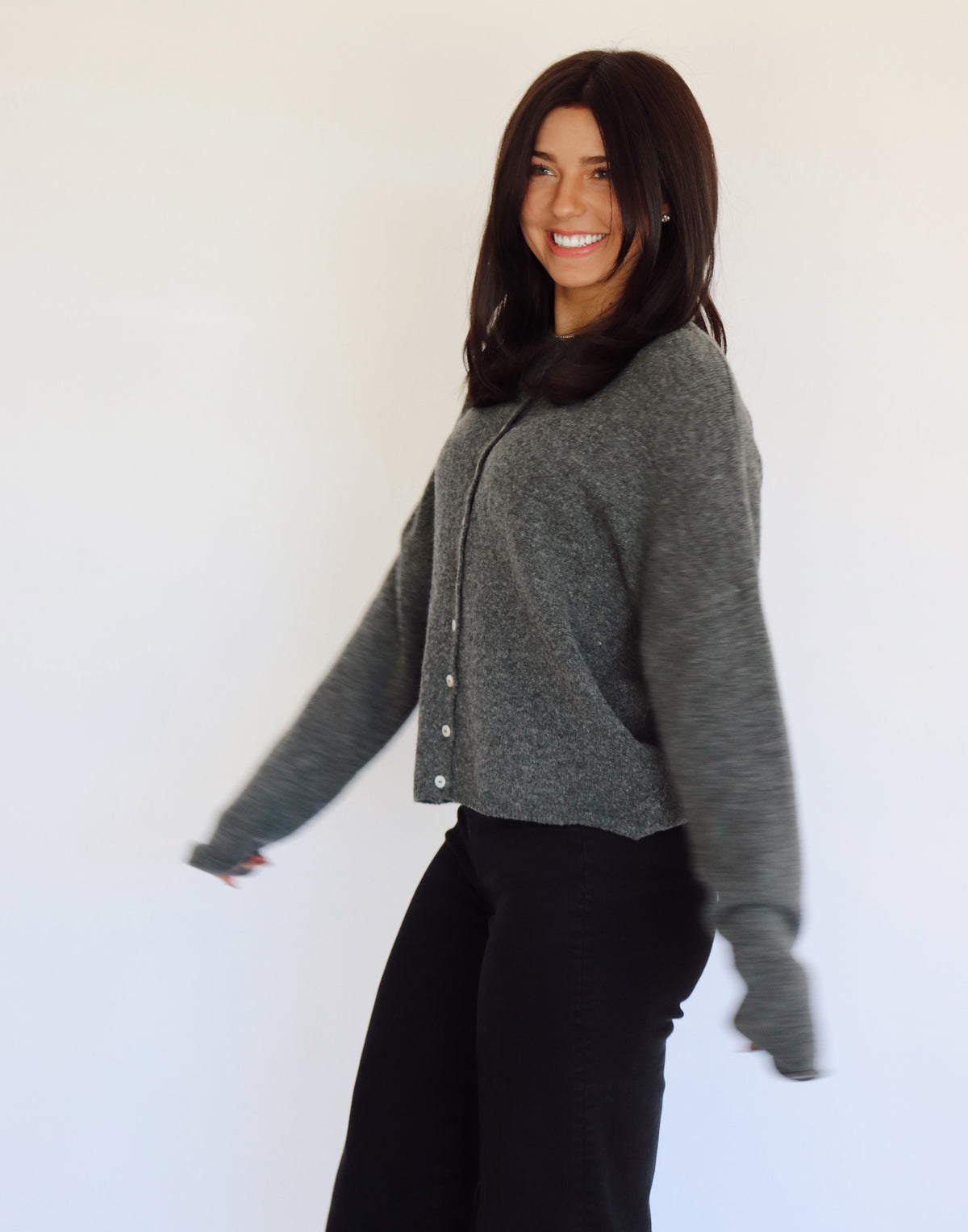 Woman wearing a gray sweater cardigan with button details against a white background