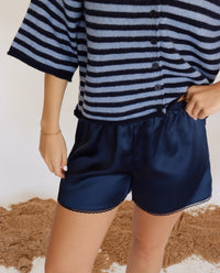 Person wearing a striped shirt and navy shorts on a neutral background