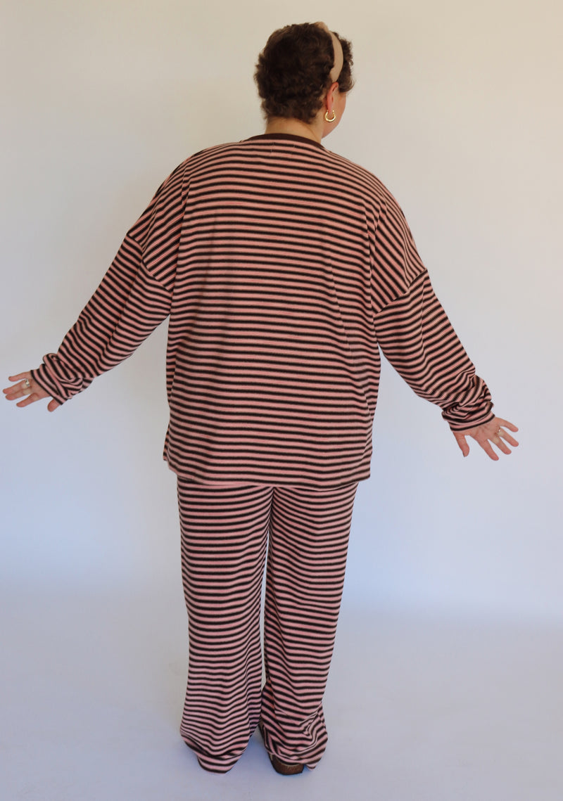 Woman wearing a brown and pink striped loungewear set in front of an off white wall.