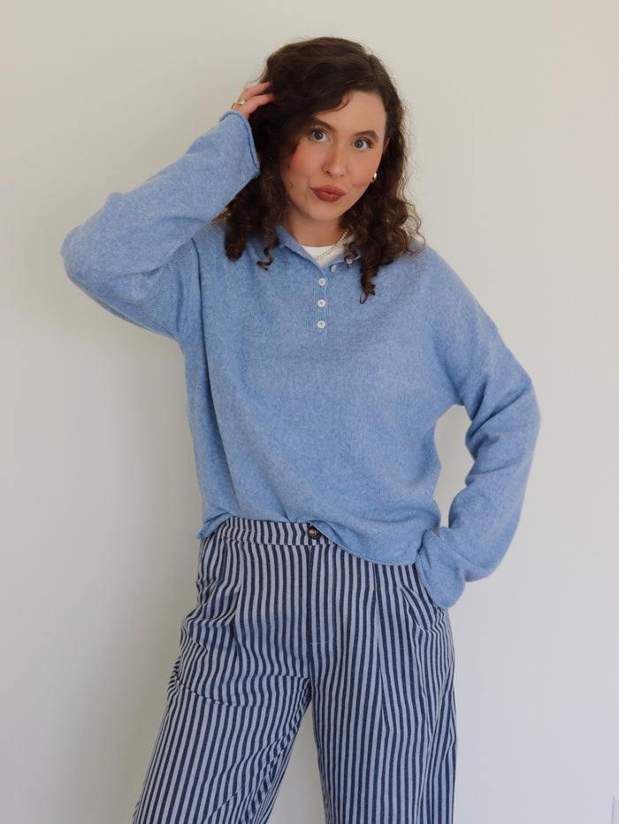 Person wearing a blue henley and striped pants against a plain background