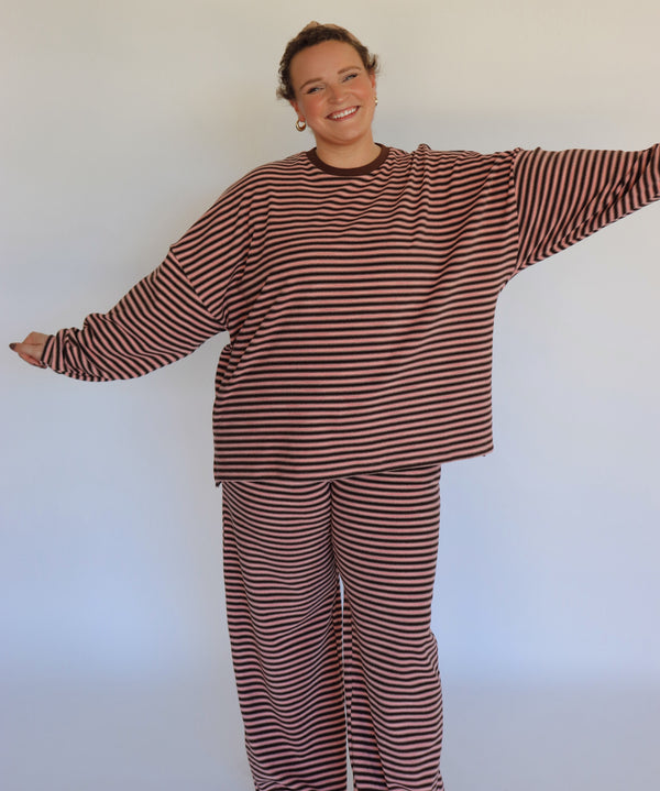 Woman wearing a brown and pink striped loungewear set in front of an off white wall.