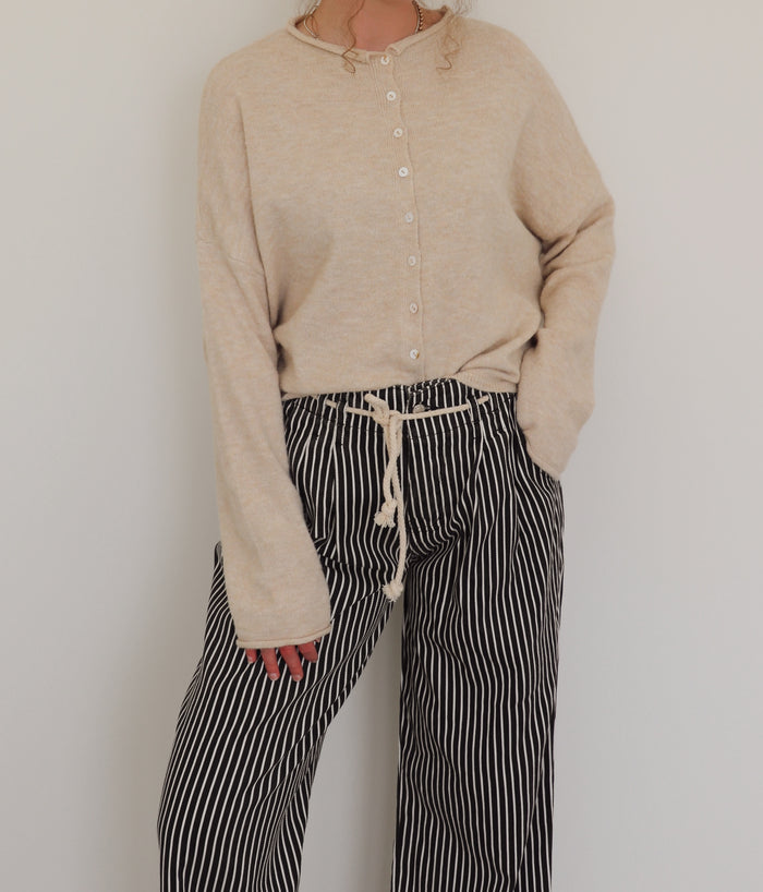 Person wearing a beige cardigan and black and white striped pants against a plain background