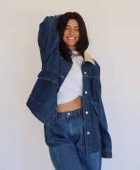 Person wearing a blue denim jacket and denim pants against a white background