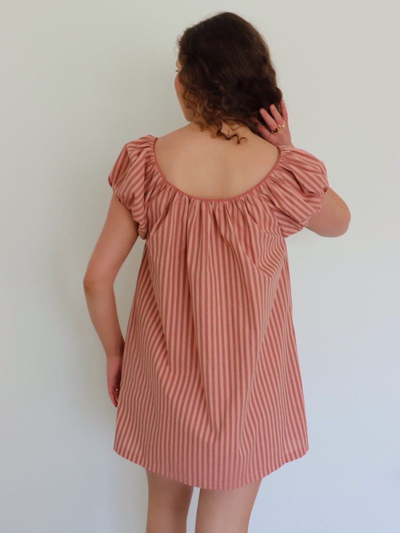 Woman wearing a peach striped dress against a plain background