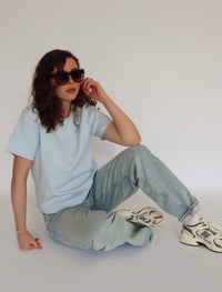 Woman wearing a light blue tee shirt and denim in front of a white background 