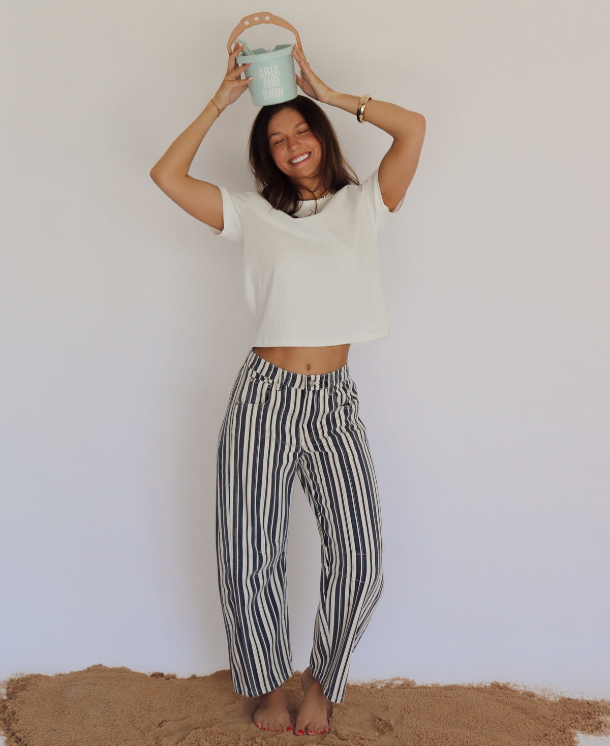 Person wearing a white top and striped pants holding a small bucket against a plain background