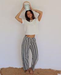 Person wearing a white top and striped pants holding a small bucket against a plain background